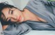 A woman laying on a bed in a gray robe.