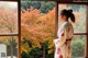 A woman standing in front of a window looking out at the trees.