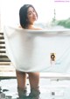 A woman in a bathtub with a towel over her head.