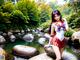 A woman in a red and white outfit standing on a rock by a river.